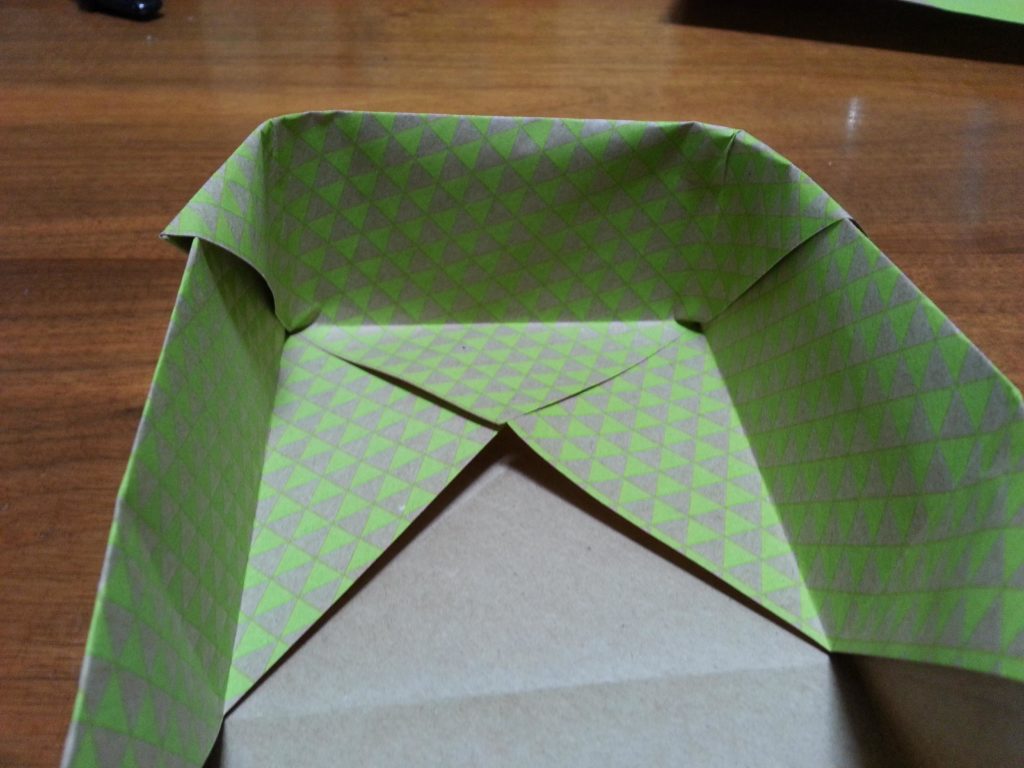 Open up the sides and fold the top end in. The first time is a little tricky, but think of how gift box corners fold in.