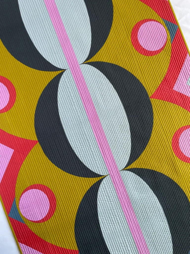 Close up of gold, blue, lavendar, pink and red quilt by Jen Wagner