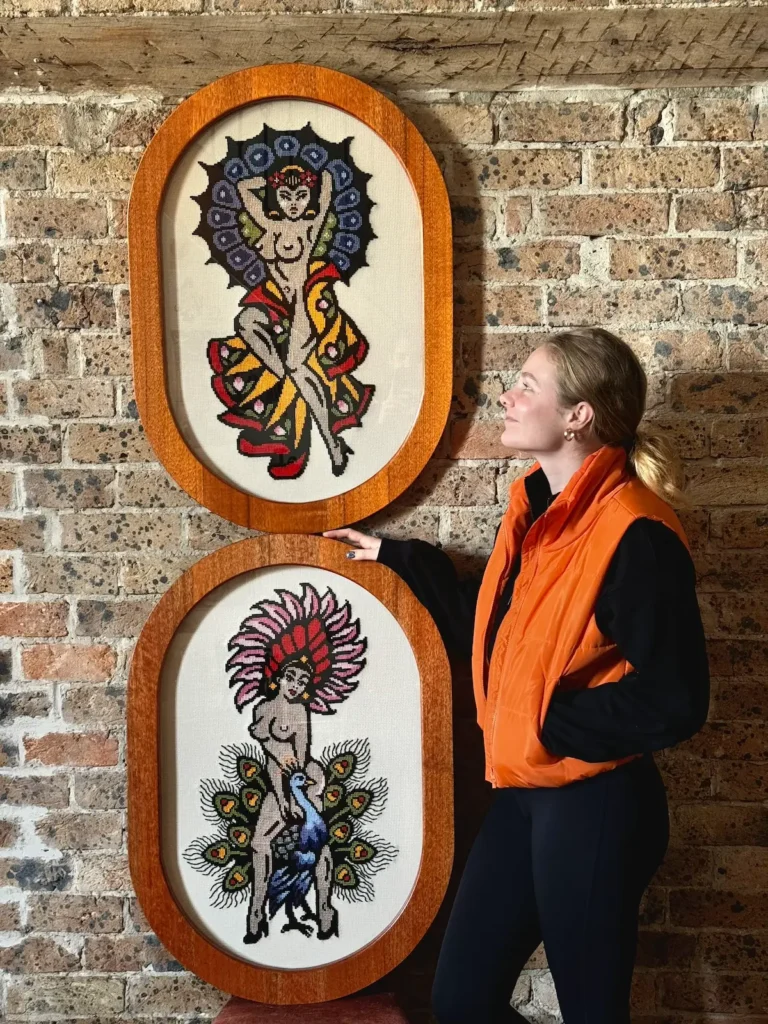 Maddie Jones with two large finished cross stitches featuring goddesses