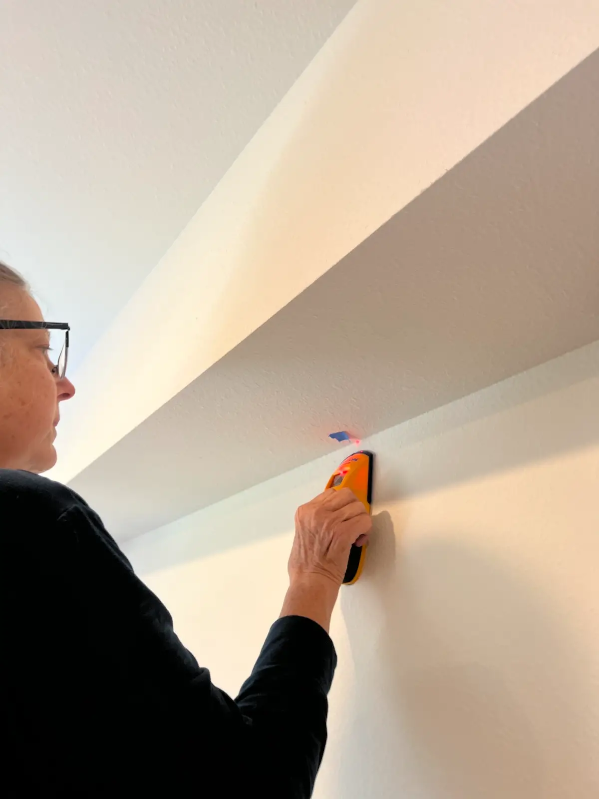 Marking the studs for the design wall with a piece of painters tape on the ceiling