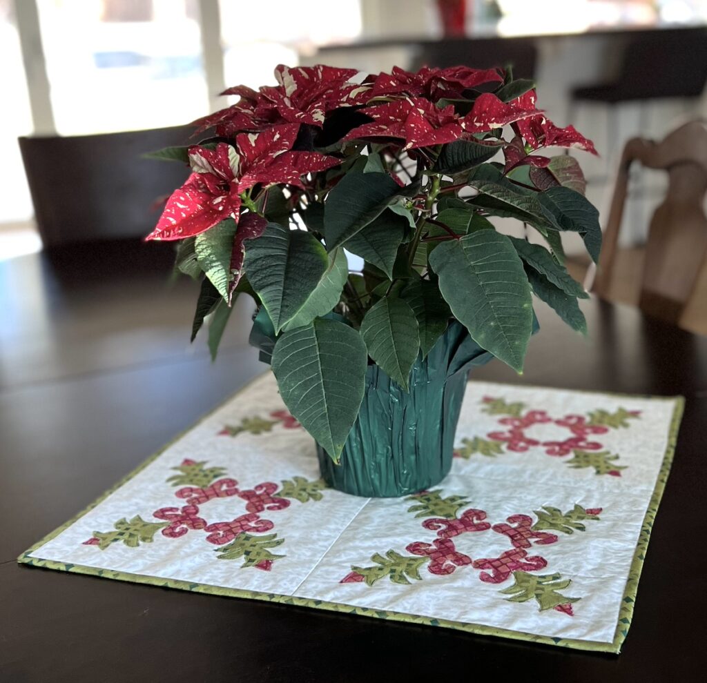 Christmas cactus applique quilt on a table with a poinsetta