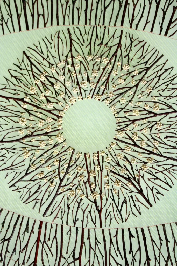 Showing work in progress of adding the flowers to the twigs on the green tulle by Olga Prinku