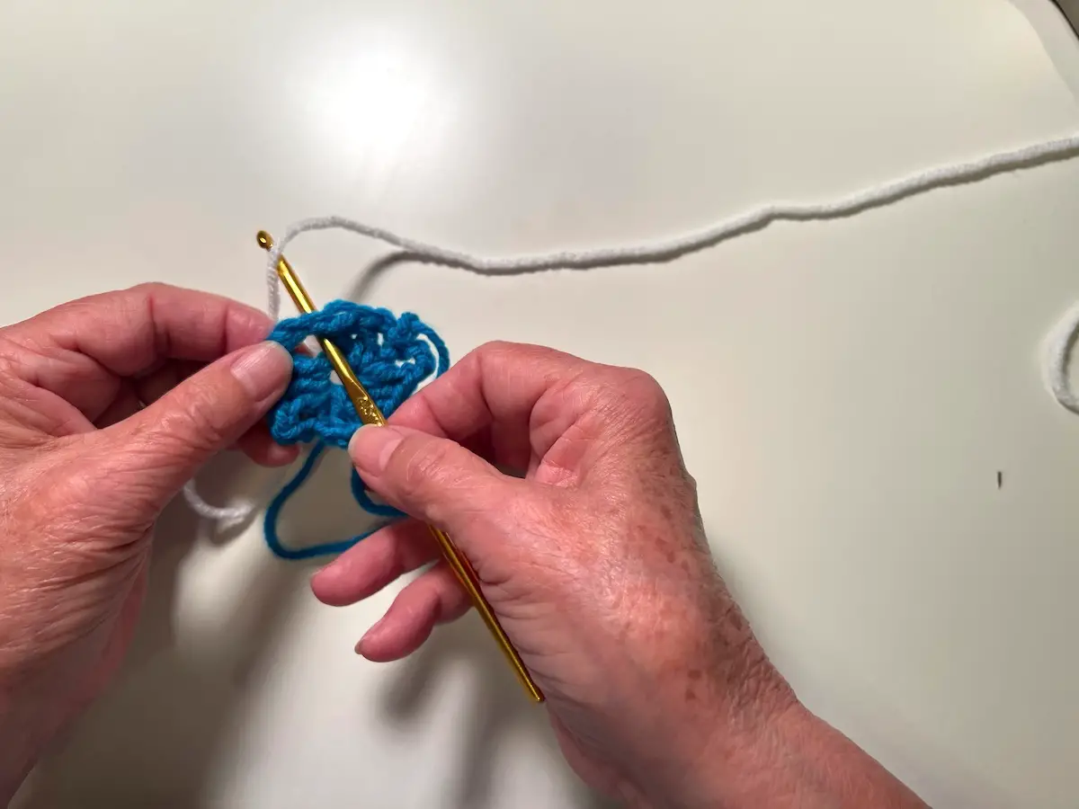 Now it's time to add a new yarn for the second round of the granny square. Put your hook through one of the openings and bring a loop of the next yard through