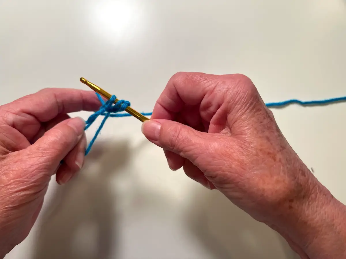 Now there are three stitches on the hook. Wrap the yarn around the hook and bring it through the first two stitches for the double crochet for the granny square