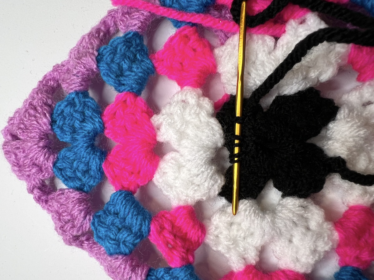 On the wrong side of your granny square, use the needle to split the yarn. Pick up about 5 threads.