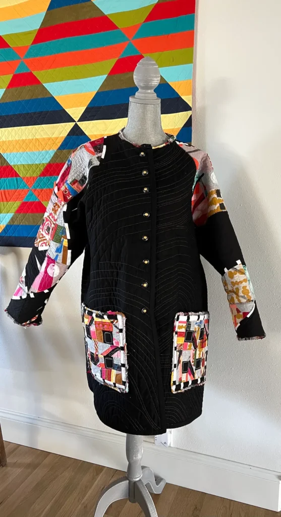 Black art quilt coat in front of a bold color quilt