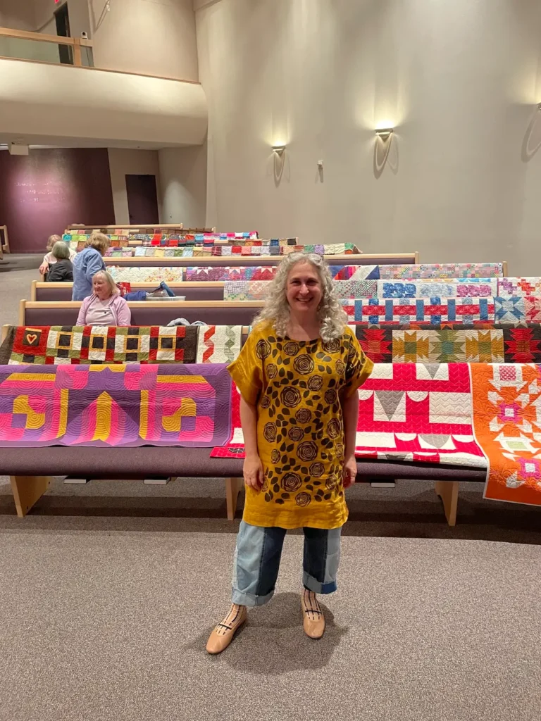 Michelle Freedman with a lot of her quilts behind her
