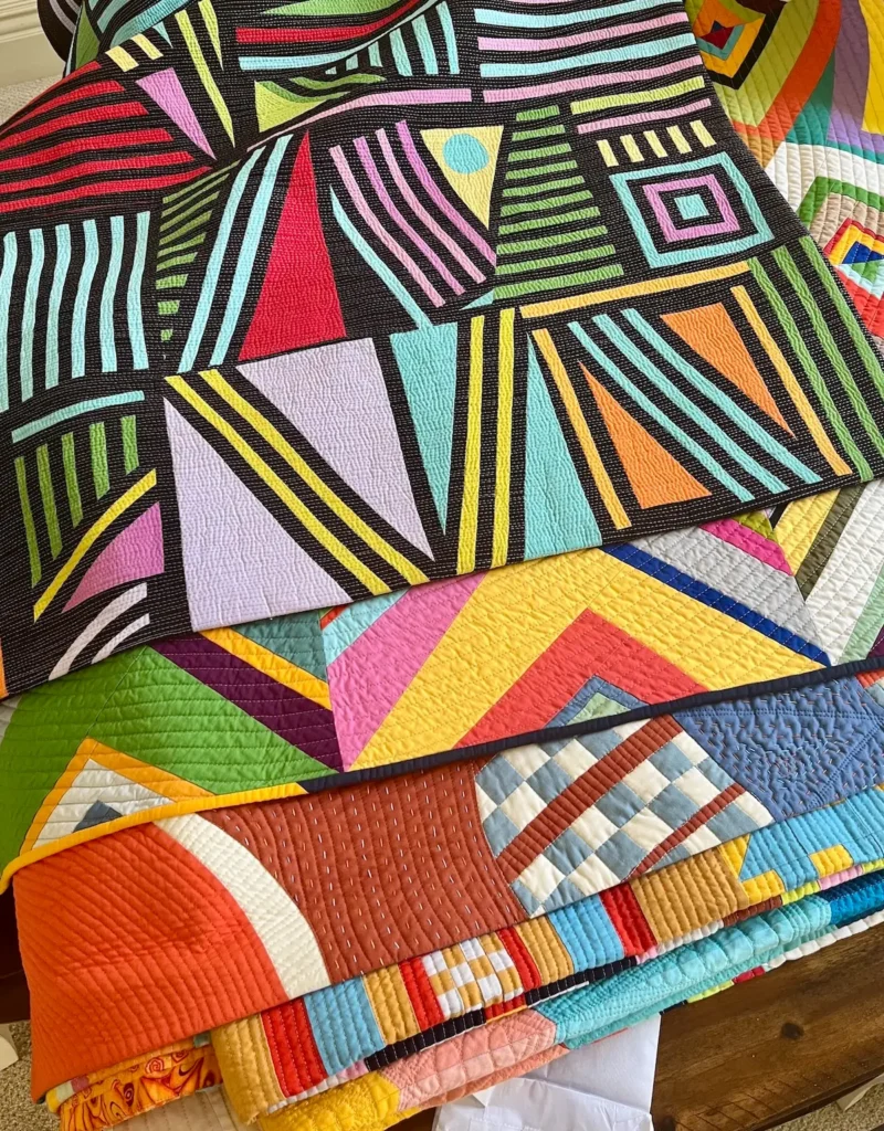Quilts by Candi Lennox stacked for a trunk show