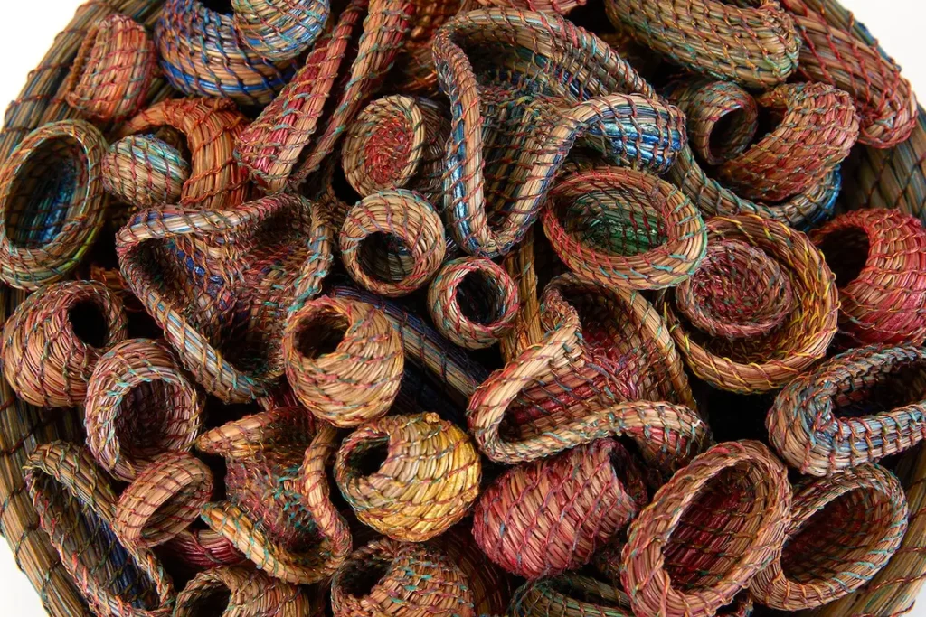 Top down view of many small pine needle baskets in a large basket all woven by Clay Burnette
