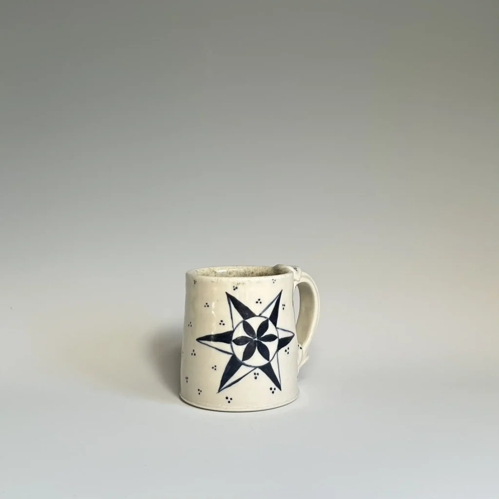 Big star with a flower in the middle on the front of a pottery mug made by Summer Brendlinger