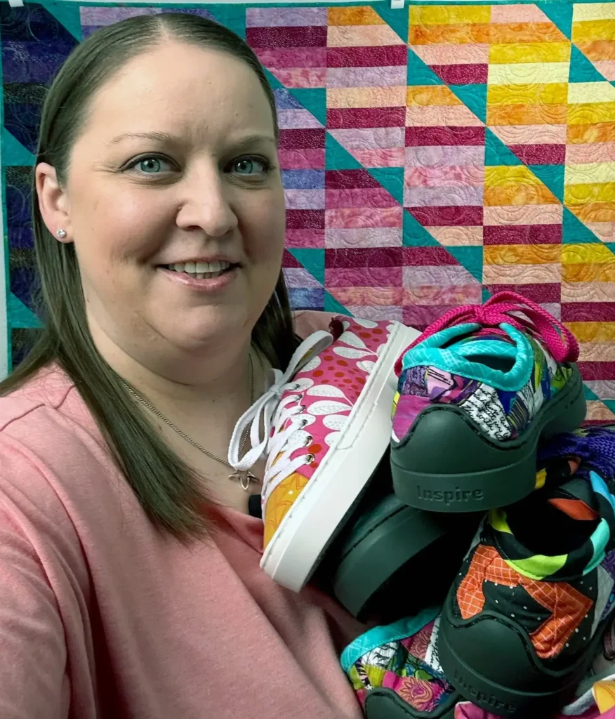 Natalie Buxkemper with a quilt behind her holding a pile of patchwork kicks that she made